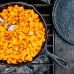 Butternut squash in a cast iron skillet cooking over a campfire