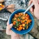 Michael holding a bowl of stew near a campfire