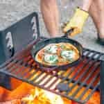 Michael placing a cast iron skillet pizza over the campfire