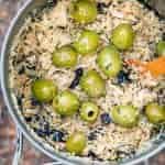 A wooden spoon in a pot that is filled with couscous and green olives