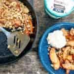 Apple crisp in a blue bowl next to a cast iron skillet