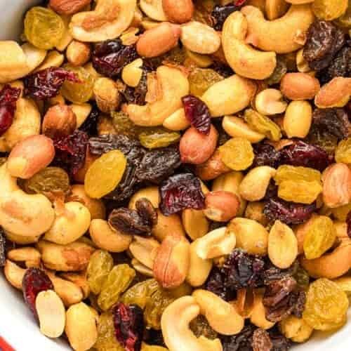 A close-up shows a bowl containing assorted nuts and dried fruits, such as cashews, peanuts, raisins, golden raisins, and dried cranberries.